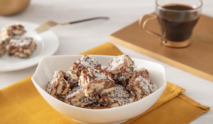 Foto da receita de Palha Italiana de Café. Observa-se um recipiente branco com as palhas dispostas e, atrás, um copinho de café para acompanhar.
