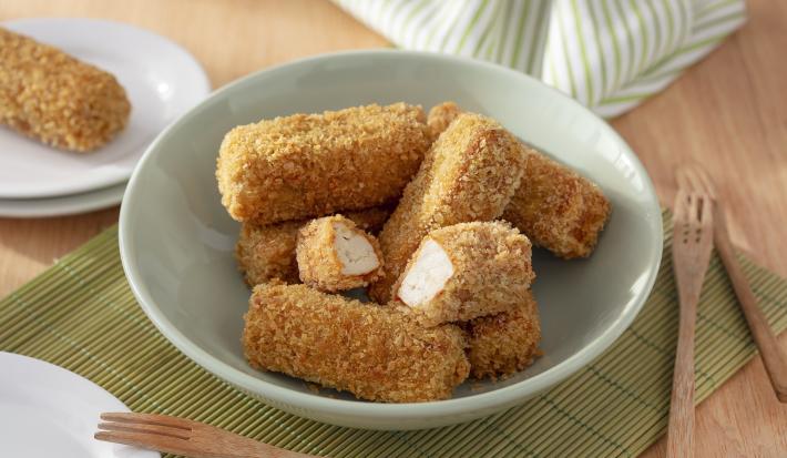 Foto da receita de Bolinho de Tofu. Observa-se uma tigela de porcelana verde clara com os bolinhos empanados dentro, sendo que um está cortado no meio. A tigela está sobre uma rede de sushi e uma superfície de madeira.