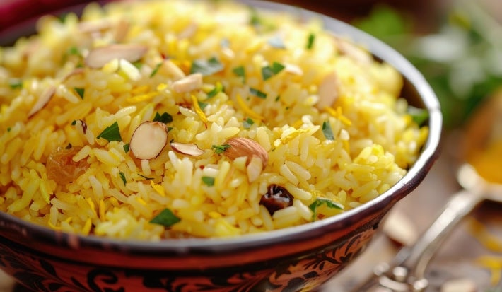 Em cima de uma mesa, tigela redonda com porção de arroz amarelo e soltinho com amêndoas picadas, decorado com salsinha picada.