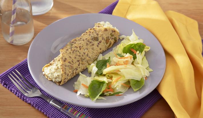 Fotografia em tons de lilás com um prato lilás ao centro e uma toalha amarela. Dentro do prato existe uma receita de wrap com sementes de chia e abóbora recheado com um creme de ricota com Ninho e acompanhado de uma salada.