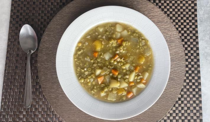 Imagem da receita de Sopa de Ervilha com Legumes, em um prato branco, sobre uma mesa e ao lado uma colher