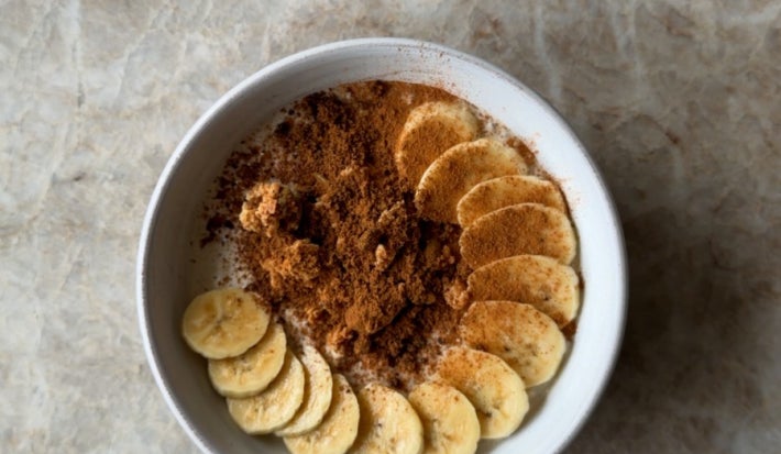 Fotografia de um pote branco com mingua de aveia dentro e rodelas de banana com canela decorando