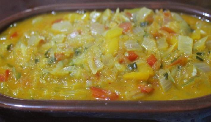 Fotografia de uma moqueca de ovo e mamão verde dentro de um recipiente escuro.