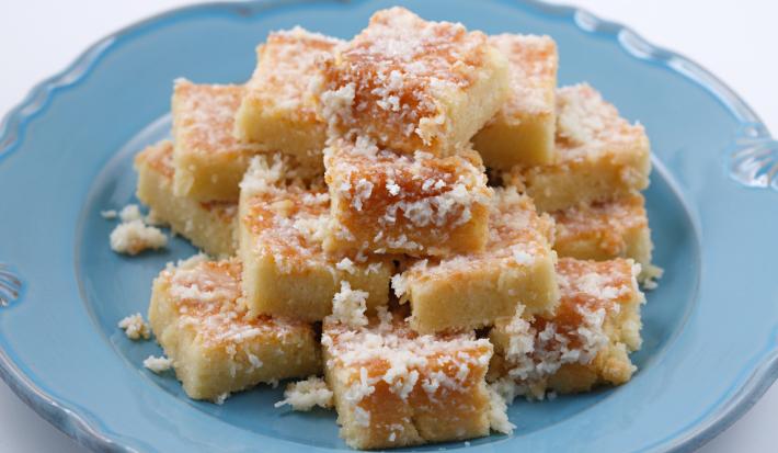 Imagem de um prato azul com pedaços quadrados do bolo coberto com coco empilhados.