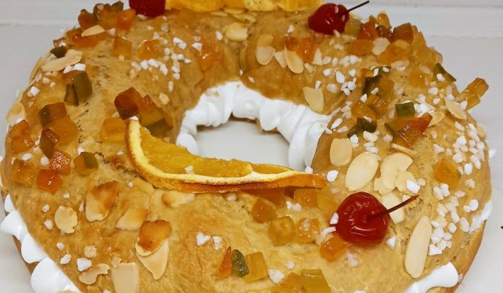 Foto da receita de Rosca de Reis. Observa-se uma rosca recheada com chantilly e decorada com frutas secas, cereja e amêndoas laminadas.