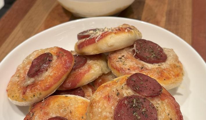 Fotografia de várias mini pizzas dentro de um prato de vidro branco fundo sobre uma tábua de madeira.
