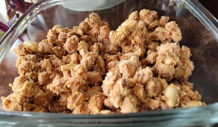 Foto em tons de bege da receita de amendoim perfumado servida em uma travessa de vidro retangular sobre uma mesa de madeira