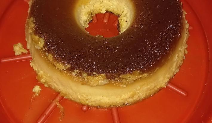 Fotografia de um pudim de pão feito na air fryer, sobre um apoio grande, e fundo vermelho.
