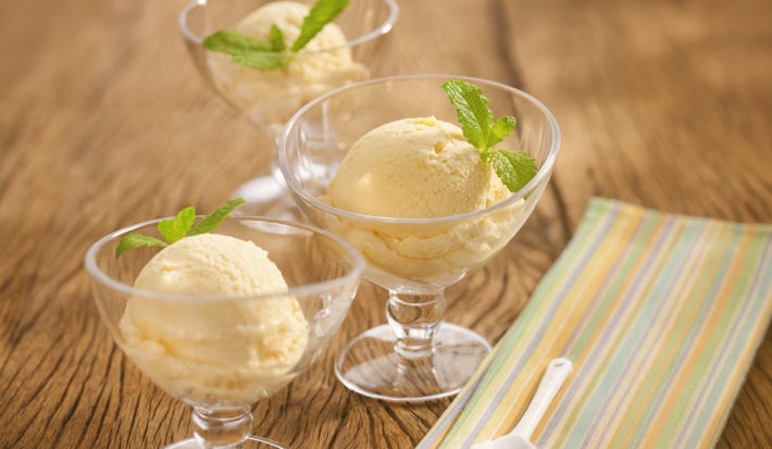 Em uma mesa de madeira contém duas taças de vidro com uma bola de sorvete cada.