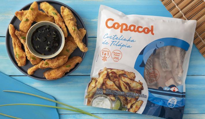 Foto da receita de Costelinha de Tilápia Copacol Empanada com Molho Oriental na Airfryer, servida em um tigela azul escura, com um pote pequeno com o molho no centro do prato, tudo numa bancada azul e com o pacote do produto Copacol