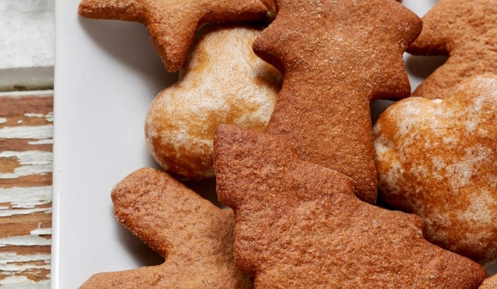 Em cima de uma mesa, prato com biscoitos em formato de estrelas e árvores de Natal.