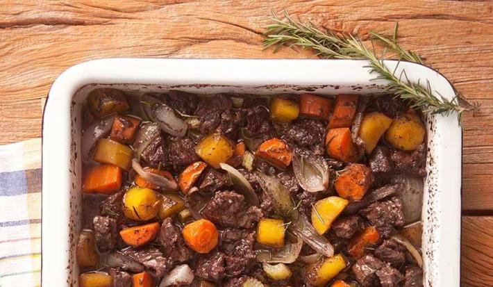 em uma mesa de madeira contém um recipiente com o picadinho com cenoura, mandioquinha e salsão.