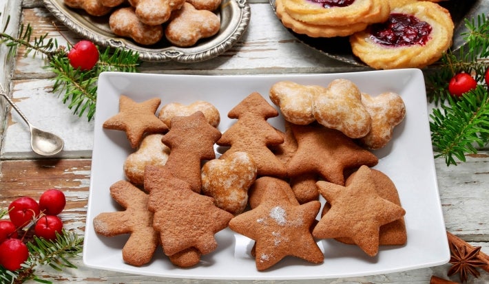 Em cima de uma mesa, prato com biscoitos em formato de estrelas e árvores de Natal.