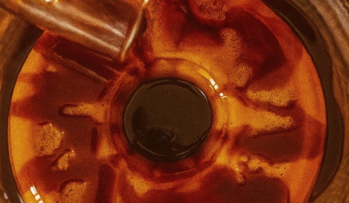 Fotografia vista de cima de um flan com uma calda de chocolate sendo despejada por cima.