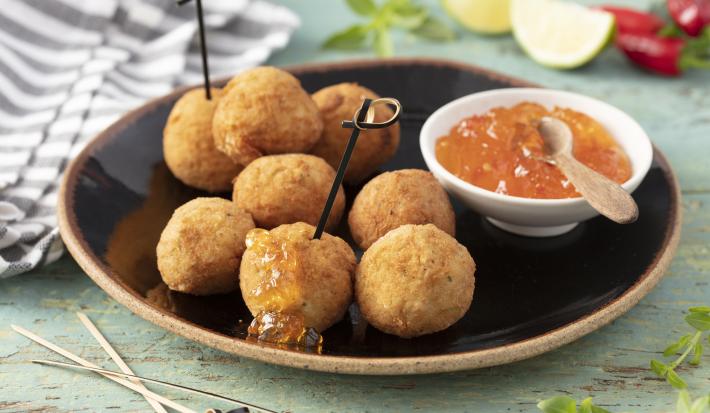 Imagem de um prato rústico preto com bolinhos de arancini e um potinho com geleia de pimenta.