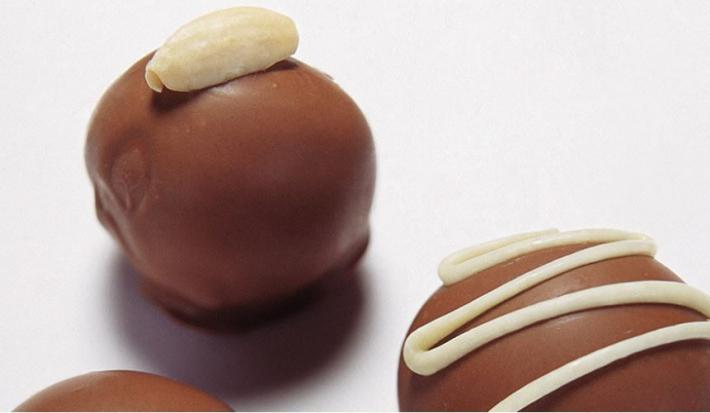 fotografia em tons de branco e marrom de uma bancada branca vista de cima que contém 3 bombons de chocolate