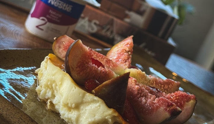 Fotografia de uma receita de iogurte assado com pedaços de figos por cima. A sobremesa está em um apoio retangular, e ao fundo tem uma embalagem do NESTLÉ Iogurte Natural Zero Lactose.