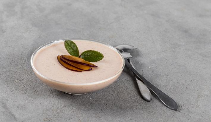 Fotografia em tons de branco em uma bancada de madeira de cor cinza. Ao centro, uma taça contendo a mousse com duas colheres ao lado.