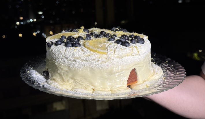 imagem mostra um bolo de massa clara com pontinhos roxos e um creme aveludado branco por cima