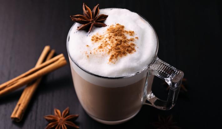 Fotografia de uma xícara de vidro com uma bebida quente com leite MOÇA, chocolate em pó, NESCAFÉ, leite, cravo, canela.