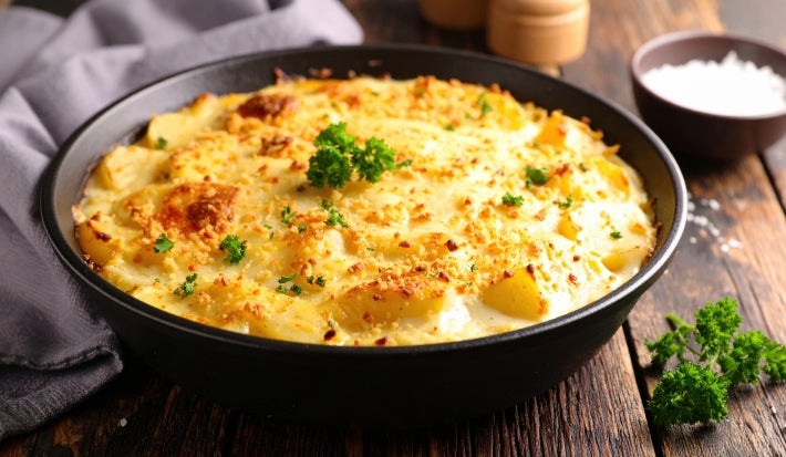 Em cima de uma mesa, refratário redondo com molho cremoso e queijo gratinado, decoado com florete de brocólis.