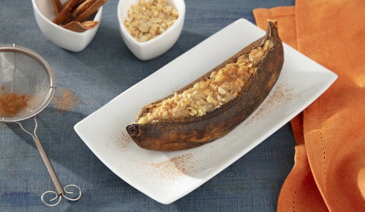 Fotografia em tons de laranja com um prato branco ao centro. Em cima do prato existe uma receita de banana assada coberta com pedaços de amendoim e polvilhada com canela