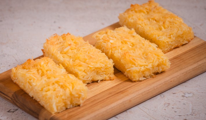 Fatias de bolo de macaxeira com coco ralado servidas em tábua de madeira