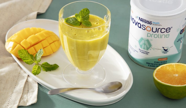 Fotografia em tons de amarelo com um pote de vidro ao centro. Dentro do pote existe uma receita de mousse de manga com laranja. Ao lado existe um pote de Novasource Proline