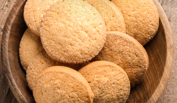 Imagem de pequenos biscoitinhos dispostos sobre um prato fundo de madeira, tons de dourado, amarelo e marrom.