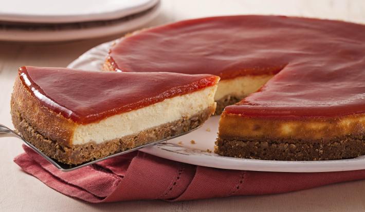Fotografia em tons de branco e rosa de uma bancada branca com um paninho rosa, sobre ele um prato branco com torta de goiabada. Ao fundo dois pratos brancos.