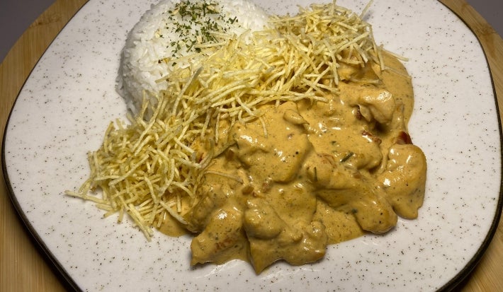 Fotografia de um prato de vidro branco com uam receita de estrogonofe de sobrecoxa com arroz e batata palha.