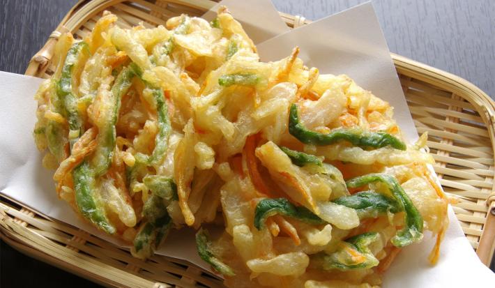 Imagem de uma cesta de palha com um tempurá de legumes frito.