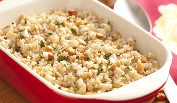 fotografia em tons de vermelho e bege tirada de uma tábua marrom com um recipiente em tons de vermelho e branco com arroz dentro.