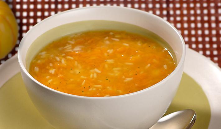 Fotografia em tons de vermelho e laranja em uma mesa com uma toalha vermelha, um prato redondo fundo com a sopa de abóbora dentro dele.