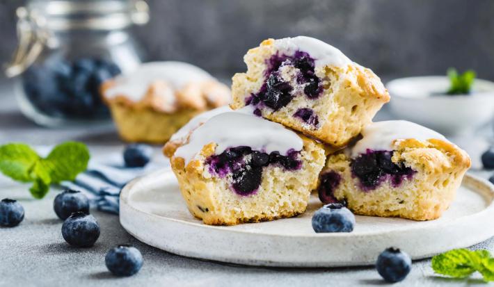 Fotografia em tons de branco com três bolinhos cupcakes ao centro. Os cupcakes são feitos com blueberries e cobertura de limão.