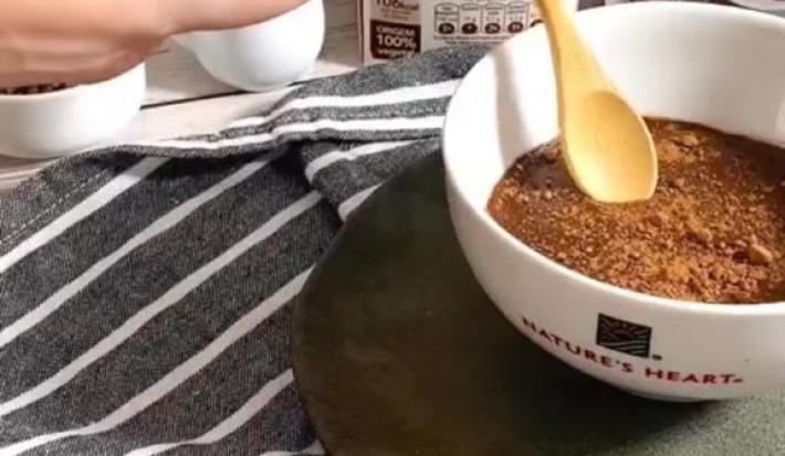 Foto da receita de Brigadeiro Plant-based. Observa-se uma tigela branca com o brigadeiro de colher dentro e as embalagens de Natures Heart atrás.