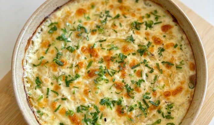 Visto de cima, prato de porcelana bege com queijo gratinado, decorado com cheiro-verde picado.