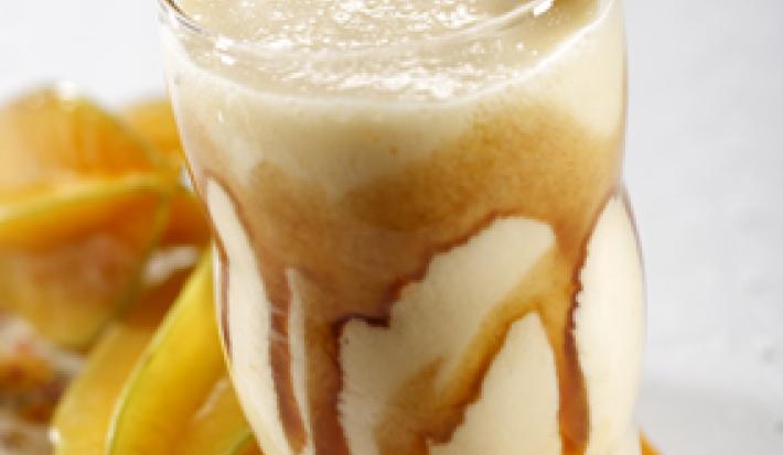 foto tirada de um copo transparente com bebida de carambola e sorvete com calda de caramelo. Ao fundo carambolas.