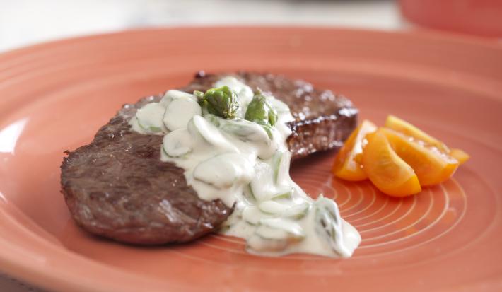 Um prato redondo e rosa visto de frente contém um pedaço de carne com molho branco por cima.