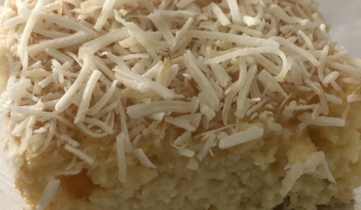 Pedaço de bolo gelado de coco coberto com coco ralado, sobre papel-alumínio em superfície clara.