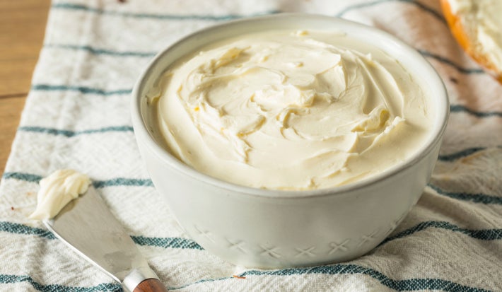 Fotografia mostra um requeijão servido em um pote branco sobre um pano listrado.