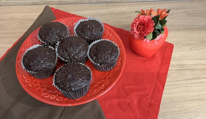 Fotografia em tons de marrom com vermelho com um prato vermelho ao centro. Em cima do prato existe vários muffins feitos de banana, aveia e nescau