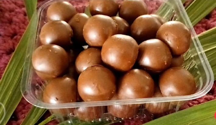 Fotografia de uma embalagem quadrada de plástico com vários bombons pequenos e redondos de açaí.