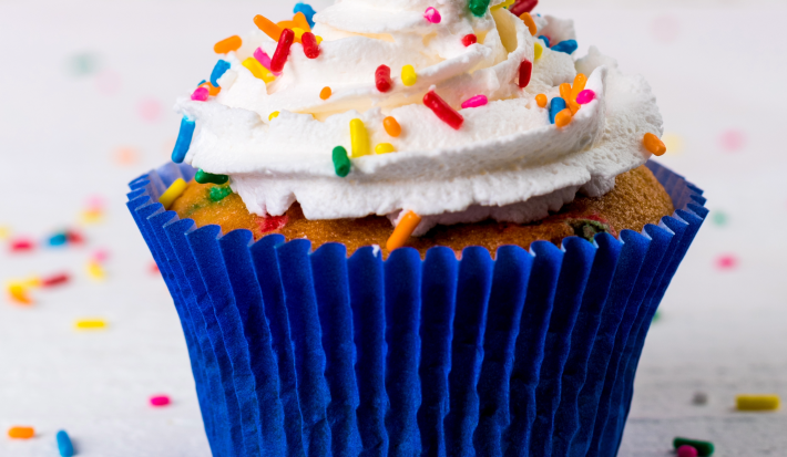 Imagem de um cupcake em forma branca, decorado com chantily branco e granulados coloridos.