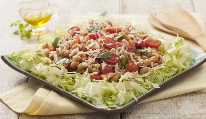 Fotografia em tons de verde em uma bancada de madeira clara com um pano amarelo e um prato quadrado verde com a salada de soja em cima dele. Ao fundo, um potinho com azeite.