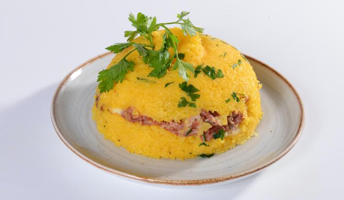 Foto da receita de Cuscuz Recheado de Calabresa. Observa-se um cuscuz recheado no prato com folhas de coentro em cima.