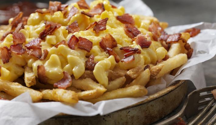 Fotografia de uma porção de batatas fritas cobertas por queijo cheddar e pedaços de bacon.