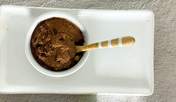 Foto em tons claros de cinza da receita de mousse de cacau com 3 ingredientes servida em um bowl de porcelana branco sobre uma base de porcelana de mesma cor.