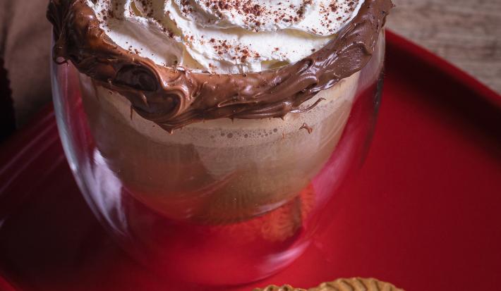 Foto vista de cima da receita de cappuccino avelã servida em um copo de vidro sobre uma louça vermelha