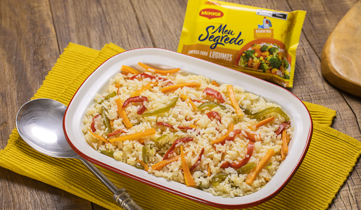 Fotografia mostra uma travessa com arroz com pimentões coloridos e uma colher servindo arroz.